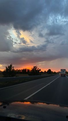 the sun is setting on an empty highway with clouds in the sky and trees to the side