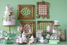 a table topped with lots of cakes and desserts next to framed pictures on the wall