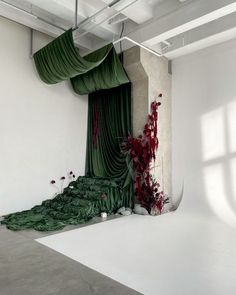 an empty room with green curtains and flowers on the floor in front of a white wall