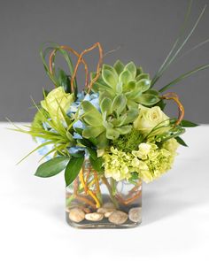 a vase filled with green and white flowers on top of a table next to rocks