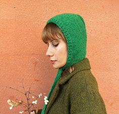 a woman wearing a green knitted hat and holding a small white flower in her hand