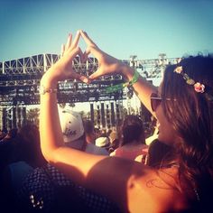 two people making the shape of a heart with their hands at an outdoor music festival