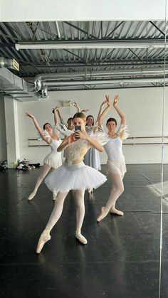 ballet students in white tutus and leotards with their arms raised, posing for the camera