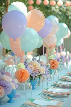 there are many balloons and flowers on the table at this birthday party that is decorated with pastel colors