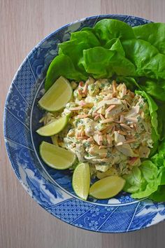 a blue and white bowl filled with lettuce, chicken salad and limes