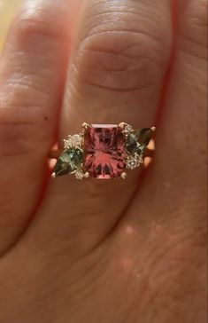 a woman's hand holding an engagement ring with pink and green stones