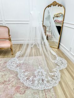 a white wedding veil on top of a rug in front of a mirror and chair