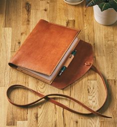 a brown leather notebook sitting on top of a wooden floor next to a potted plant