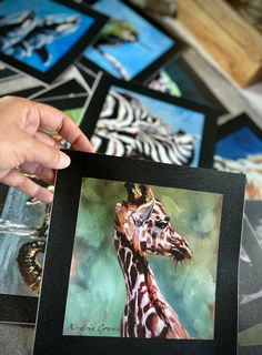 a person holding up a painting of a giraffe in front of other pictures