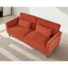 an orange couch sitting on top of a carpeted floor next to a white wall