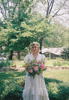 a woman in a white dress holding a bouquet of flowers and wearing a flower crown