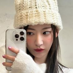 a woman holding up her cell phone in front of her face and wearing a knitted hat