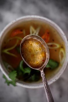 a close up of a spoon in a cup filled with soup and veggies