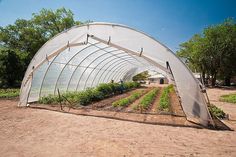 a large green house sitting in the middle of a dirt field with plants growing inside