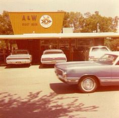 two cars parked in front of a fast food restaurant with an aw sign above it