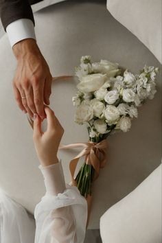 the bride and groom are holding hands on their wedding day, with white flowers in front of them