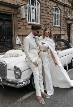 a man and woman standing next to each other in front of a white wedding car