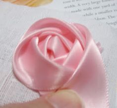 a person is holding a pink rose on top of a piece of paper with an open book in the background