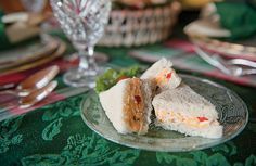 two sandwiches on a glass plate with silverware and other food items in the background