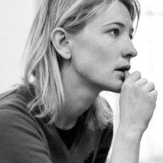 a black and white photo of a woman with her hand on her chin looking off to the side