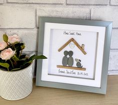 a white vase filled with pink roses next to a framed picture and a small potted plant