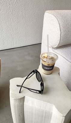 a cup of coffee sitting on top of a white chair next to a pair of sunglasses