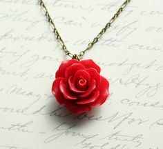 a necklace with a red rose on it sitting on top of a piece of paper