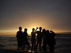 a group of people standing in the ocean at sunset