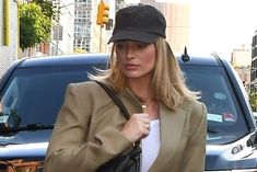 a woman walking down the street with a black purse in her hand and a hat on top of her head