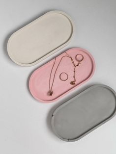 two oval trays with necklaces and earring hooks on them, one in white and the other in pink