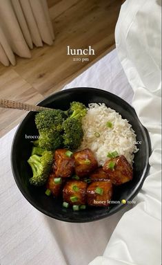 a black bowl filled with rice and broccoli on top of a white table cloth