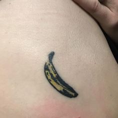 a small banana tattoo on the side of a woman's right thigh, it is black and yellow