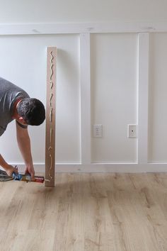 a man working on the floor in an empty room with wood floors and white walls