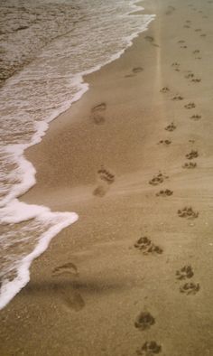 two footprints in the sand next to an ocean beach with waves coming in and one person walking along