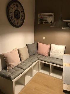 a corner couch with several pillows on it in front of a large clock mounted to the wall