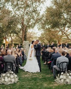 a bride and groom kissing in front of an audience at their outdoor wedding ceremony on the lawn