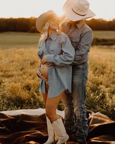 a man and woman standing next to each other on a blanket in the middle of a field