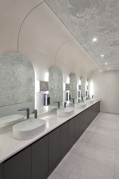 a long row of sinks in a bathroom with mirrors on the wall and lights above them