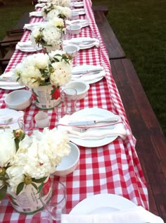 a long table is set with white and red checkered tablescloths, silverware, and flowers