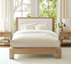 a bed with white sheets and pillows in front of a window, next to two nightstands