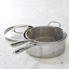 two stainless steel pots and pans sitting on a marble counter top with one holding a spatula