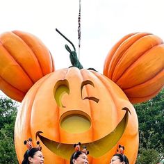 three women standing in front of a giant pumpkin with faces on it's head