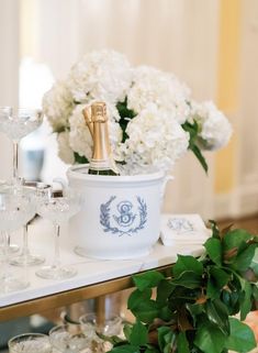 a table topped with wine glasses and white flowers next to a vase filled with greenery