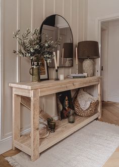 a wooden table topped with a mirror and vase filled with flowers next to a lamp