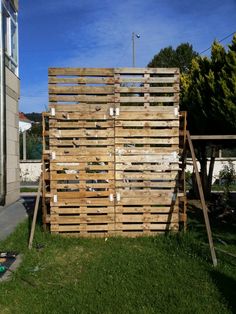 a tall wooden structure sitting in the grass next to a building with windows on it