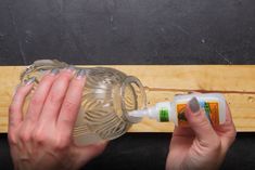 two hands are holding an empty bottle near a wooden board that is being used as a wall hanger