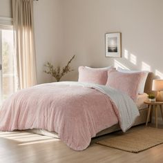 a bed with pink comforter and pillows in a bedroom next to a window,