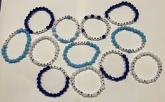 six bracelets with blue and white beads are arranged in a circle on a piece of paper