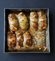 some food is in a metal pan on a black counter top and it looks like they have been rolled up