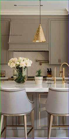 two white chairs sitting at a kitchen island with flowers in the center and gold accents